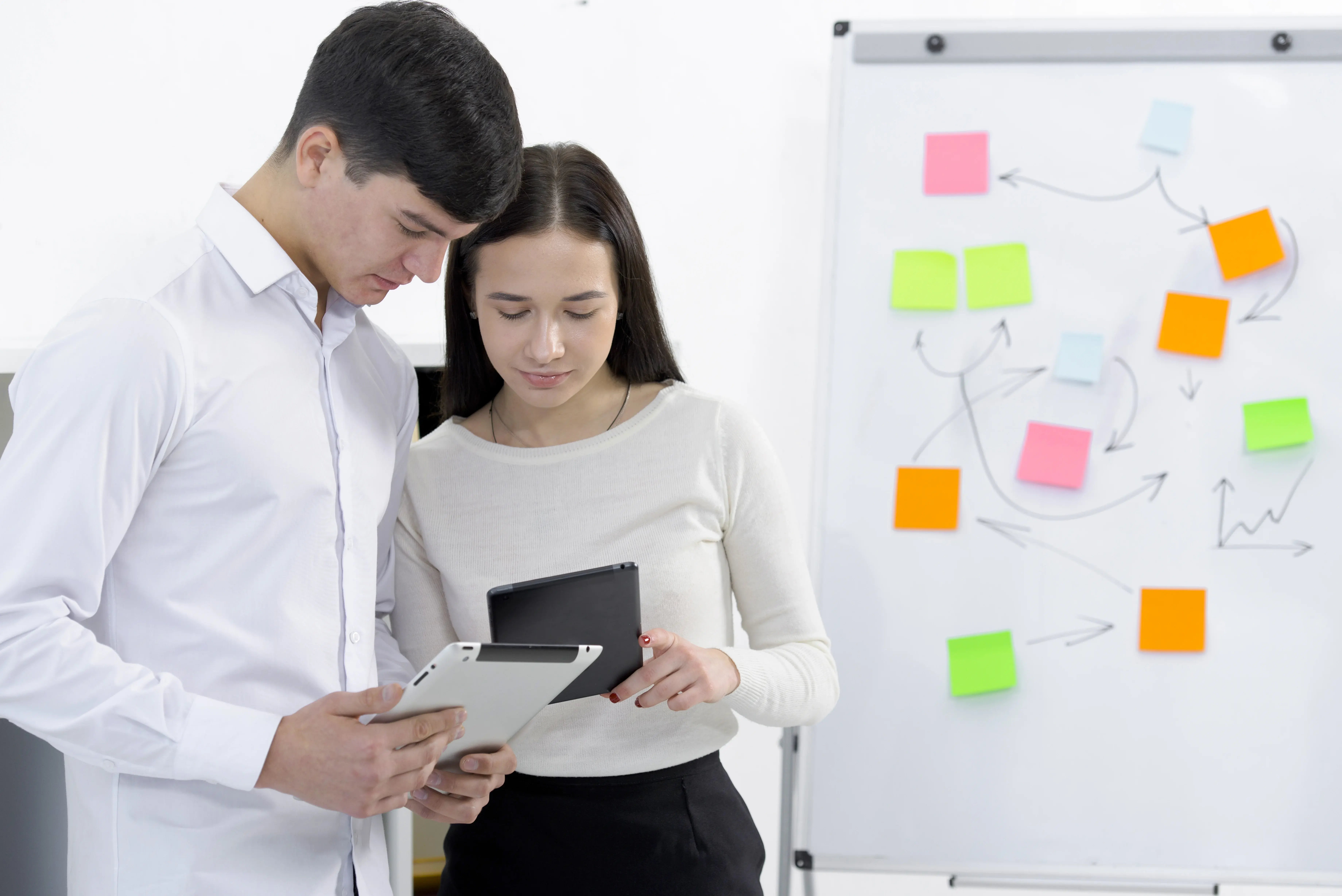 companeros-que-miran-la-tableta-digital-y-el-telefono-celular-de-pie-cerca-del-rotafolio