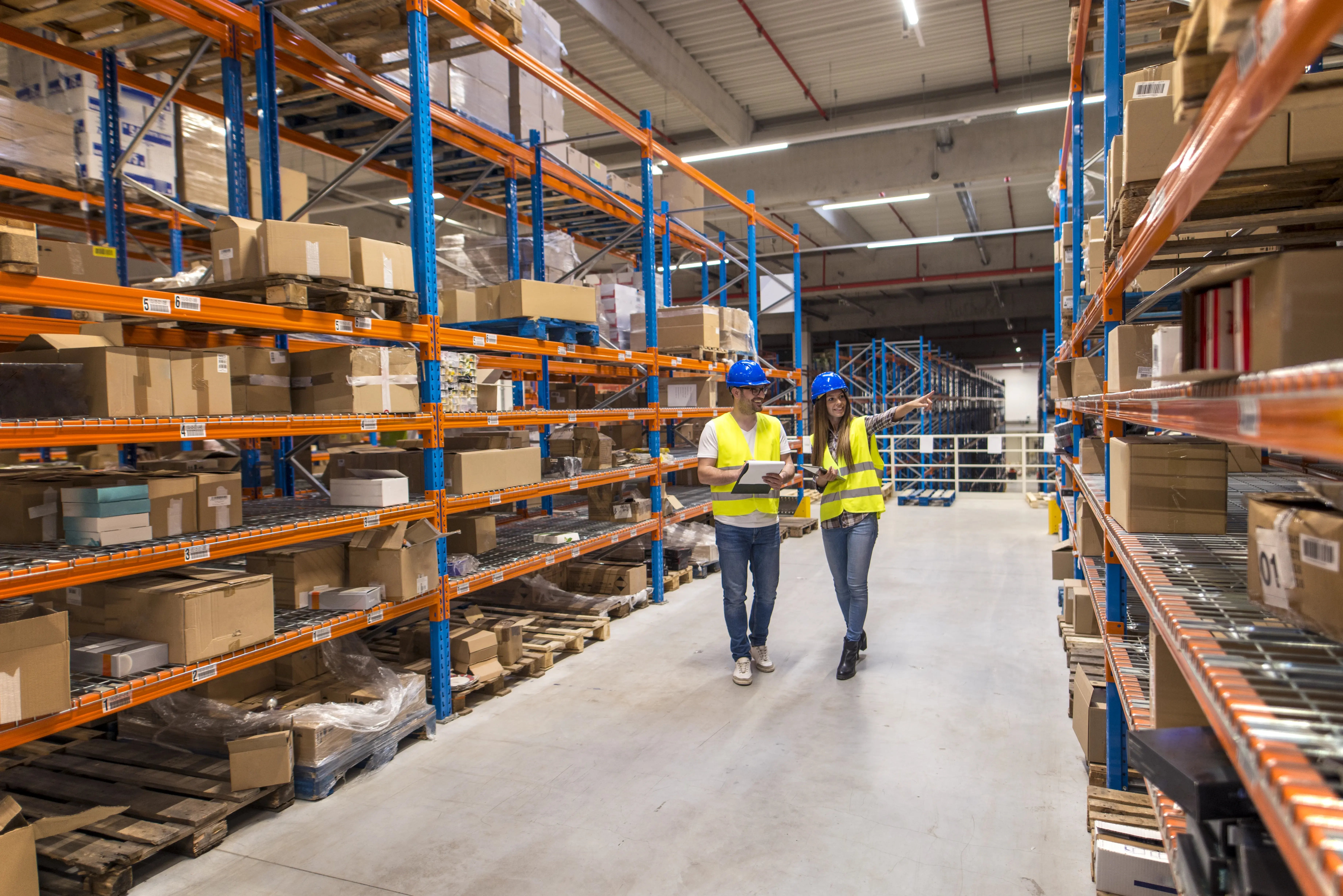 two-warehouse-workers-walking-distribution-storage-area-discussing-about-logistics-organization